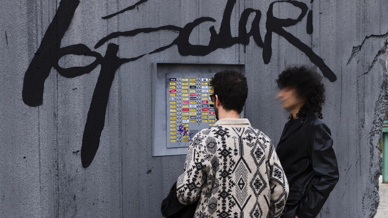 Due passanti di fronte al citofono del muro in piazza XXVI maggio