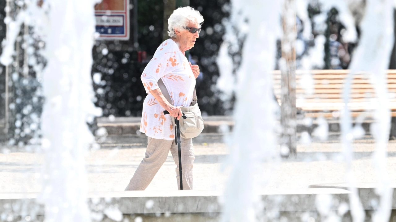 Un'anziana a spasso accanto a una fontana in centro a Milano in cerca di un minimo di refrigerio